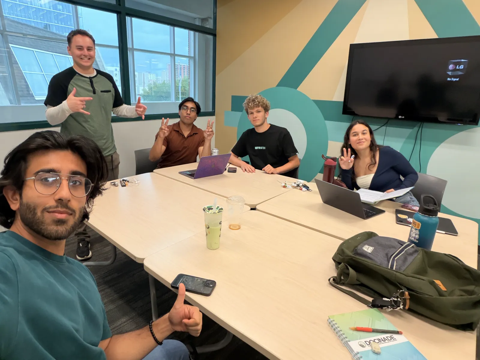 The four-person startup team and a guest around a meeting table with laptops, smiling at the camera